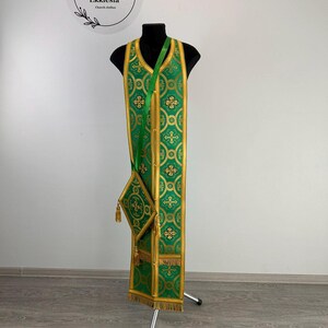 May include: Green liturgical vestment with gold embroidery and a matching green and gold pouch. The vestment is displayed on a stand.