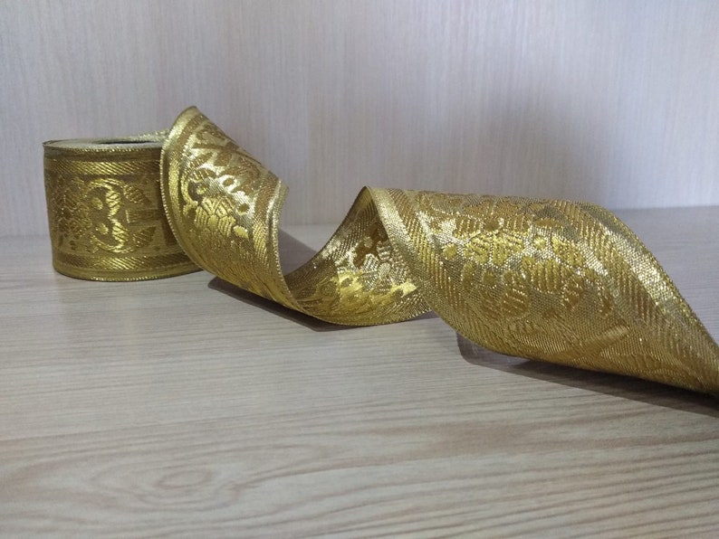 May include: Gold ribbon with a floral pattern. The ribbon is rolled up and has a shiny finish.