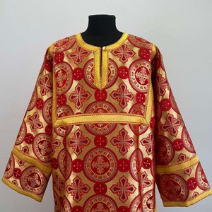 Puede incluir: Una vestimenta litúrgica roja y dorada con un patrón de cruces y círculos. La vestimenta tiene un cuello alto y mangas largas.