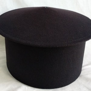 May include: A black felt hat with a round, flat crown and a tall, cylindrical brim.
