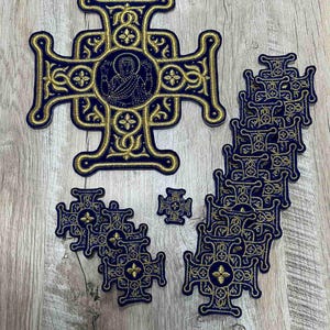 Op de afbeelding: Een set van 15 geborduurde kruisen in marineblauw met gouden draad. De kruisen zijn in verschillende maten en hebben een centraal ontwerp met een figuur in een cirkel.