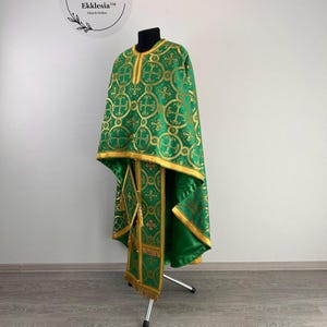 May include: A green liturgical vestment with gold embroidery, featuring a cross pattern. The vestment is displayed on a stand.