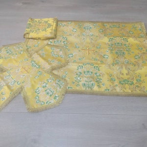 May include: A set of four yellow altar cloths with a floral pattern and gold trim. The cloths are made of a brocade fabric and have a cross design in the center.
