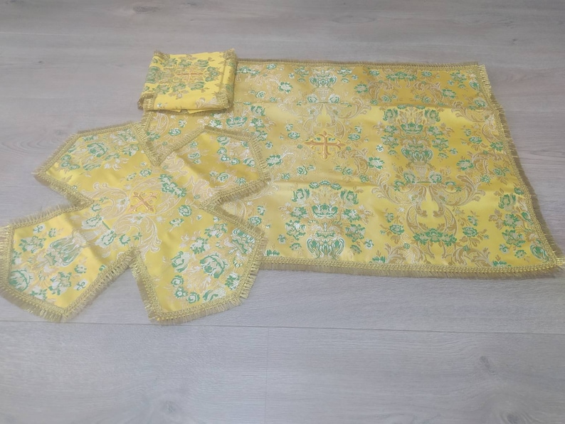 May include: A set of four yellow altar cloths with a floral pattern and gold trim. The cloths are made of a brocade fabric and have a cross design in the center.