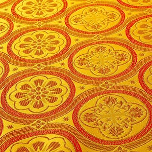 K&ouml;nnte beinhalten: Nahaufnahme eines goldenen Stoffes mit einem sich wiederholenden Muster aus roten und goldenen Kreisen. Die Kreise haben ein florales Design in der Mitte.