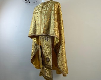 May include: A gold-colored liturgical vestment set featuring a repeating pattern of crosses within circular motifs. The garment includes a cape-like upper section and a long, narrow stole with decorative fringe and embroidered cross details.