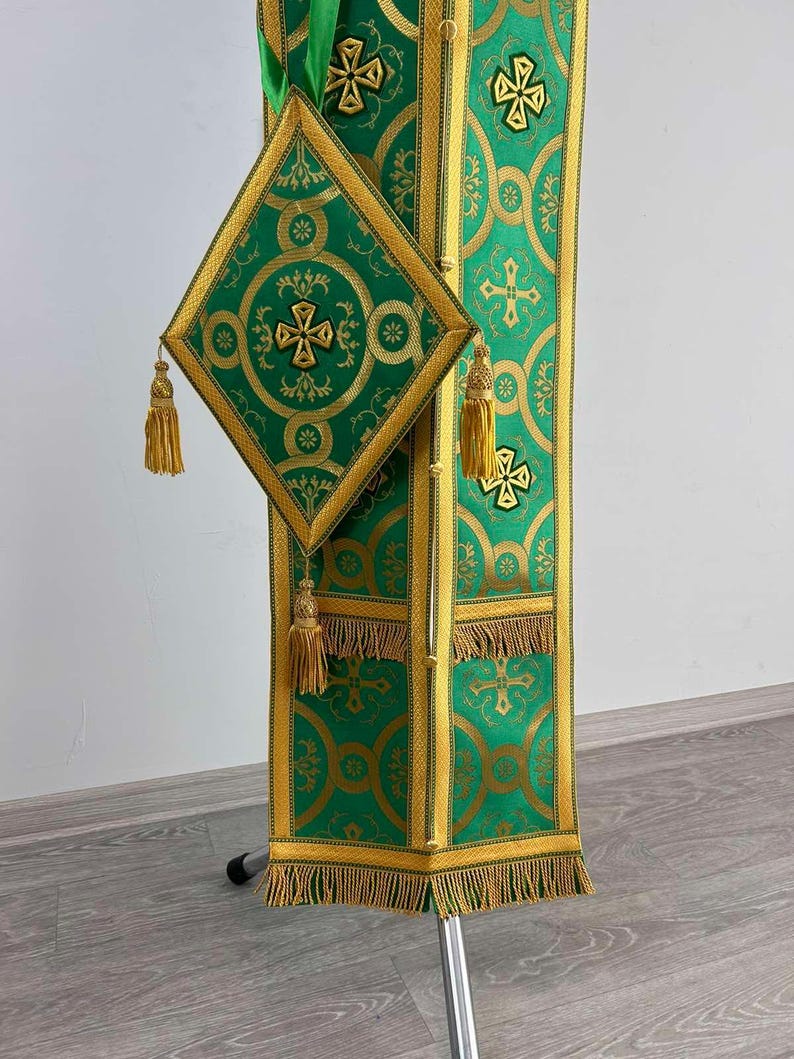 May include: A green and gold liturgical stole with a matching green and gold square pocket. The stole has a fringe trim and the pocket has a tassel.