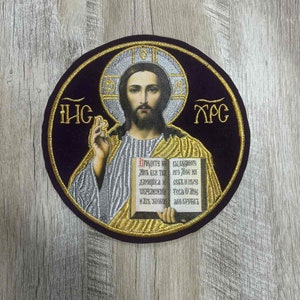 Puede incluir: Parche bordado con un icono religioso de Jesucristo sosteniendo un libro con texto en escritura cirílica. El parche es circular y tiene un borde dorado sobre un fondo de terciopelo negro.