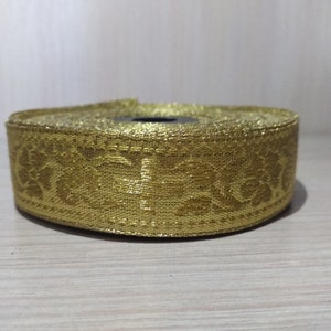 May include: Gold trim with a floral pattern. The trim is rolled up and ready to be used for sewing or crafting.
