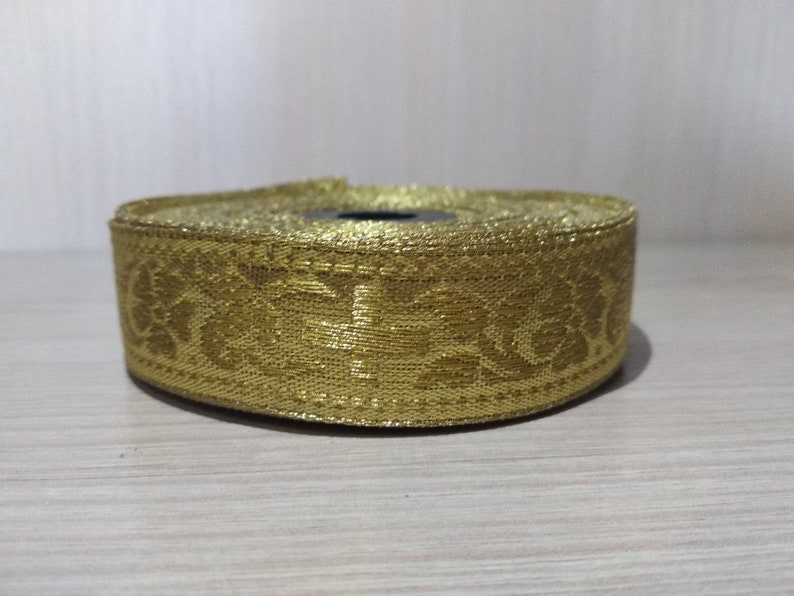 May include: Gold trim with a floral pattern. The trim is rolled up and ready to be used for sewing or crafting.