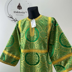 May include: Green and gold church garment with intricate patterns. The garment features long sleeves and gold trim along the neckline, cuffs, and waist. The label reads "Ekklesia Church clothes".