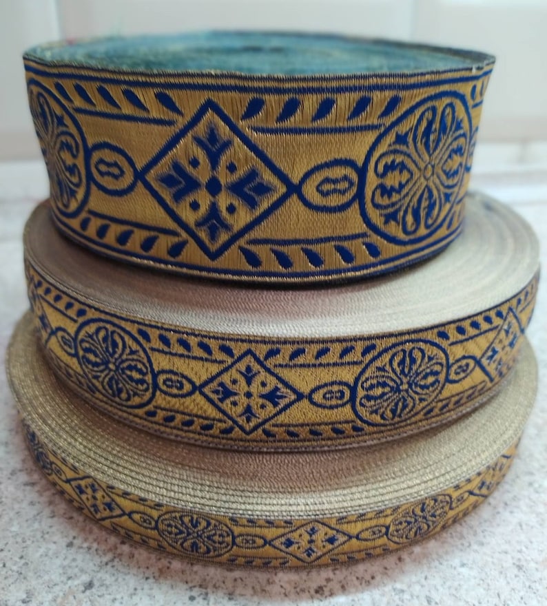 Puede incluir: Tres rollos de ribete dorado y azul con estampado. El ribete tiene un dise&ntilde;o geom&eacute;trico repetitivo con forma de diamante y motivos florales.