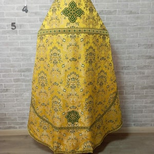 May include: A yellow and green liturgical vestment with a cross design. The vestment is made of a brocade fabric with a floral pattern.