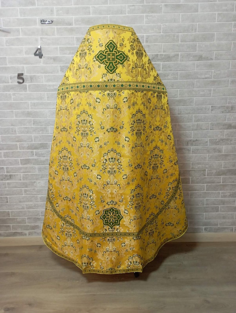 May include: A yellow and green liturgical vestment with a cross design. The vestment is made of a brocade fabric with a floral pattern.