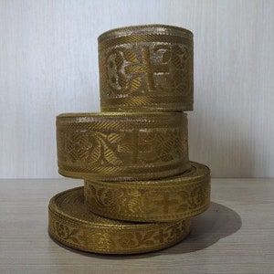 May include: Four rolls of gold trim with intricate patterns. The trim is woven with a subtle sheen and has a decorative design.