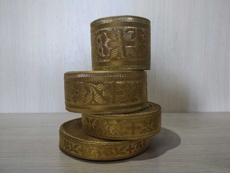 May include: Four rolls of gold trim with intricate patterns. The trim is woven with a subtle sheen and has a decorative design.