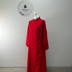 May include: A long, red robe with a mandarin collar and long sleeves. The robe has a decorative trim along the edges and a small, embroidered design on the front. The robe is made of a soft, flowing fabric.