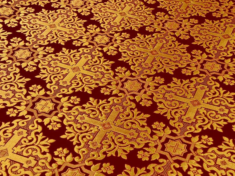 Pu&ograve; includere: Primo piano di un tessuto bordeaux con un motivo ripetuto di croci dorate, elementi floreali e disegni a forma di stella. Il tessuto ha un aspetto strutturato e una leggera lucentezza, creando un aspetto ricco e ornato. Ideale per usi religiosi o decorativi.