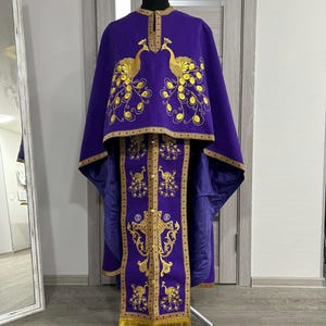 May include: A purple liturgical vestment with gold embroidery of peacocks and a cross. The vestment has a long, flowing cape and a decorative trim.