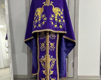 Może przedstawiać: Fioletowa szata liturgiczna z haftem złotym przedstawiającym pawie i krzyż. Szata ma długą, falującą pelerynę i ozdobny pasek.