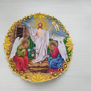 Può includere: Toppa ricamata che raffigura una scena religiosa con Gesù Cristo al centro, circondato da due angeli. La scena è ambientata su uno sfondo blu e bianco con accenti dorati.