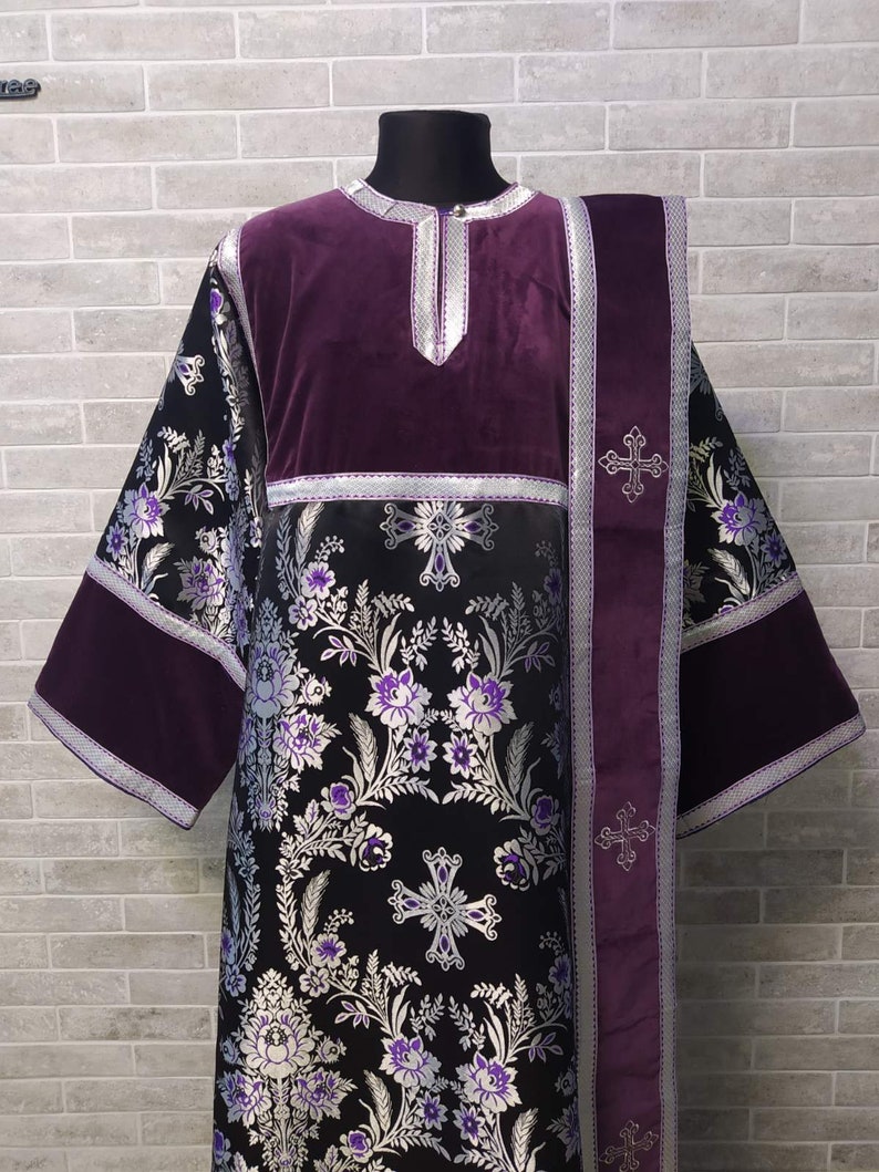 May include: A black and silver brocade liturgical vestment with purple velvet trim and a matching stole. The vestment features a floral pattern with silver crosses.
