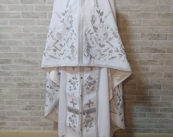 May include: White liturgical vestments with silver embroidery of grapevines and wheat. The vestments include a long robe, a shorter robe, and a stole.