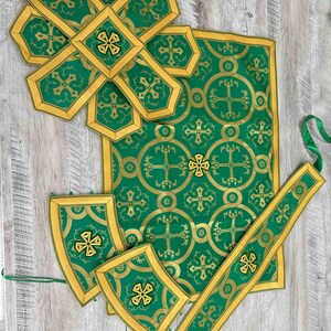 May include: A set of green and gold liturgical vestments, including a chasuble, stole, and two maniple pieces. The fabric features a repeating pattern of crosses and circles.