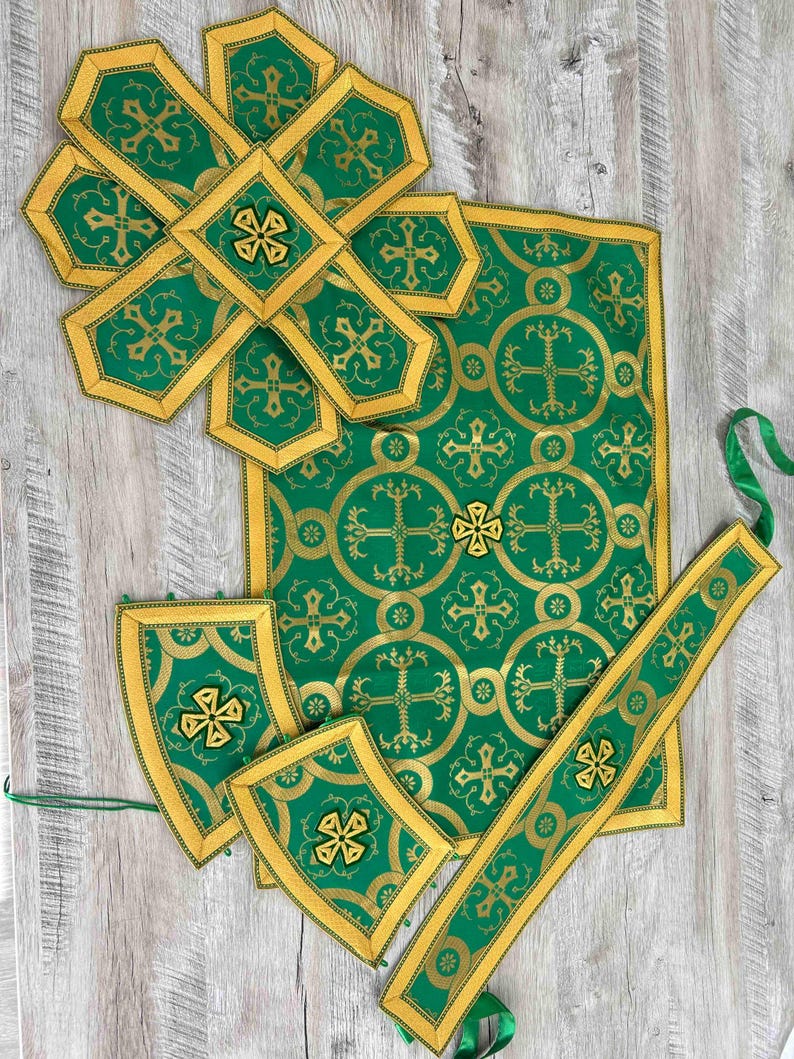 May include: A set of green and gold liturgical vestments, including a chasuble, stole, and two maniple pieces. The fabric features a repeating pattern of crosses and circles.