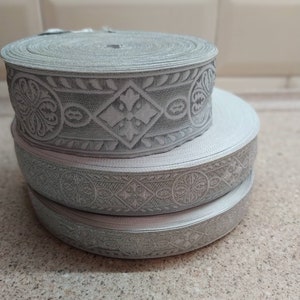 Puede incluir: Tres rollos de ribete gris plateado con un patr&oacute;n floral en relieve. El ribete est&aacute; hecho de un material suave y flexible y tiene un brillo sutil.