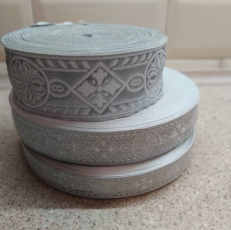 Puede incluir: Tres rollos de ribete gris plateado con un patr&oacute;n floral en relieve. El ribete est&aacute; hecho de un material suave y flexible y tiene un brillo sutil.