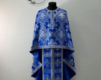 May include: A blue and silver liturgical vestment with intricate floral patterns. The vestment has a long, flowing design and is adorned with silver trim. The text "Ekklesia™ Church clothes" is visible in the top left corner of the image.
