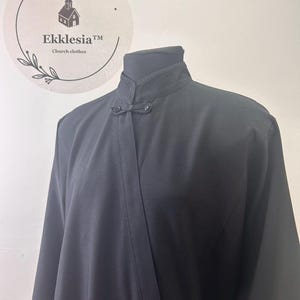 May include: A black long-sleeved shirt with a mandarin collar and button closure. The shirt has a simple design and is made of a smooth fabric.