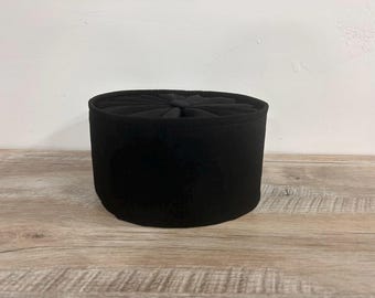 May include: A black, round, fabric hat with a folded top. The hat is sitting on a wooden surface.