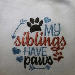Puede incluir: Un body blanco para beb&eacute; con texto bordado que dice "Mis hermanos tienen patas" con una huella de pata y flechas.