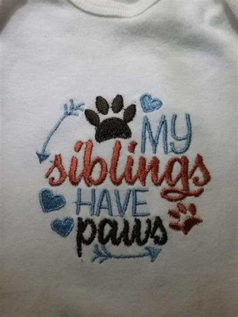 Puede incluir: Un body blanco para beb&eacute; con texto bordado que dice "Mis hermanos tienen patas" con una huella de pata y flechas.