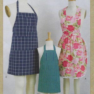 May include: Three aprons, one in a blue and white plaid pattern, one in a pink floral pattern, and one in a green and white striped pattern.  The aprons are on mannequins and the text "ADULTS' AND KIDS' APRONS" is at the bottom of the image.