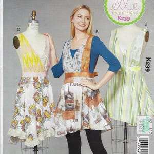 May include: A sewing pattern for aprons, featuring three apron designs. One apron has a floral print, another has a travel-themed print with the Eiffel Tower, and the third has vertical stripes. The pattern is labeled "ellie mae designs. K239".