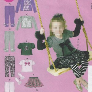 May include: A sewing pattern for girls' clothing, featuring various tops, pants, and skirts. The pattern includes a white t-shirt with a pink bow, a green top with a star design, and a purple jacket with ruffles. The image also shows a girl on a swing.