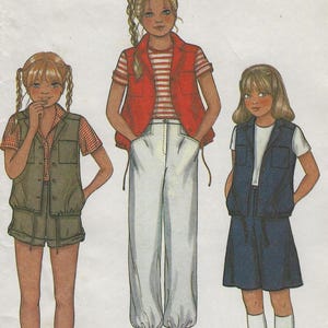 May include: A sewing pattern for three different styles of vests for girls. The pattern is from McCall's and is from a Norton Simon Inc. company. The vests are shown on three girls wearing different outfits. The first girl is wearing a green vest with a white and red plaid shirt and khaki shorts. The second girl is wearing a red vest with a white and red striped shirt and white pants. The third girl is wearing a blue vest with a white shirt and blue shorts.
