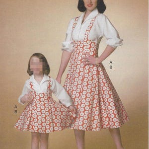May include: A vintage sewing pattern from The Archive Collection, circa 1958, featuring a mother and child in matching dresses. The dresses have a red and white floral print, white blouses, and suspender-style straps.