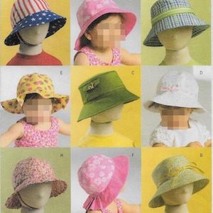 May include: A collection of nine bucket hats in various patterns and colors, including a red, white, and blue striped and star-patterned hat, a pink floral hat, a blue plaid hat, a yellow strawberry print hat, a solid green hat, and a white hat.