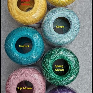 May include: Six spools of colorful crochet thread in shades of yellow, blue, green, pink, and purple. Each spool is labeled with its color name: Golden Yellow, Mimosa, Ocean, Peacock, Spring Greens, Soft Mauve, and Purple.