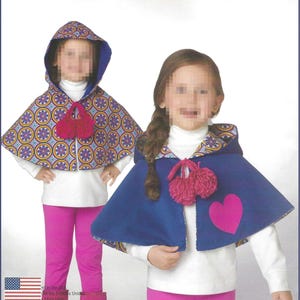 May include: Two hooded capes featuring a reversible design. One cape displays a vibrant circular geometric pattern in purple, orange, and blue, while the other is solid blue with a pink heart appliqué. Both include matching pink yarn pom-poms.