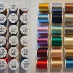 May include: A collection of colorful spools of thread, arranged in rows. The spools are labeled with numbers and text, indicating the thread type and length. The colors range from gold and silver to blue, pink, and green, suitable for sewing and crafting projects.
