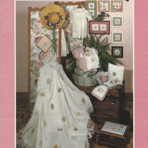 May include: A cross stitch collection titled "Granny's Attic" by Sue Hillis. The cover features a white crocheted blanket with floral embroidery, a hat, a baby dress, and a variety of framed cross stitch patterns.