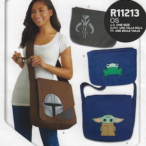 May include: A woman models a brown messenger bag with a Mandalorian helmet design. Other bags in the image include a dark gray bag with a symbol and two blue bags, one with a frog and one with Grogu. The bags are one size.