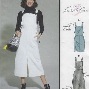 May include: A woman wearing a white overall dress with overall buckles, a black turtleneck, and black ankle boots. The dress has a front slit and side pockets. A tote bag with a leopard print is held in her left hand. The image also includes sewing pattern illustrations.