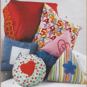 May include: A set of five pillows in various sizes and patterns. The pillows are made of different fabrics and feature a variety of designs, including numbers, hearts, and flowers. The pillows are arranged on a white surface. The text "RANGERS" is visible on one of the pillows.