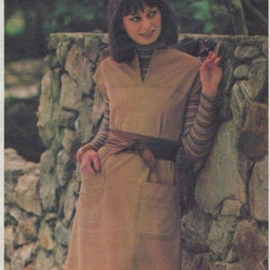May include: A woman wearing a tan pull-over jumper dress with a brown belt and pockets. The dress is paired with a striped turtleneck. The image includes the text "SEW & GO" and "The pull-over jumper".